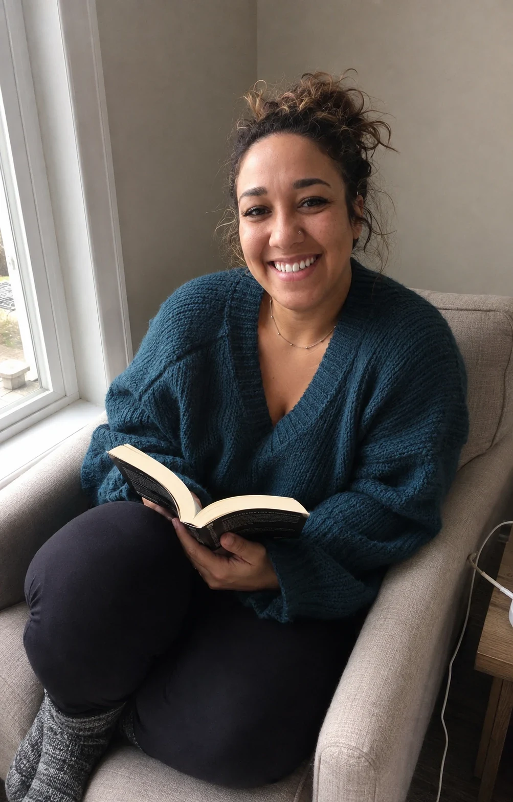 Erica Rivera in a teal sweater, holding an open book beside a window